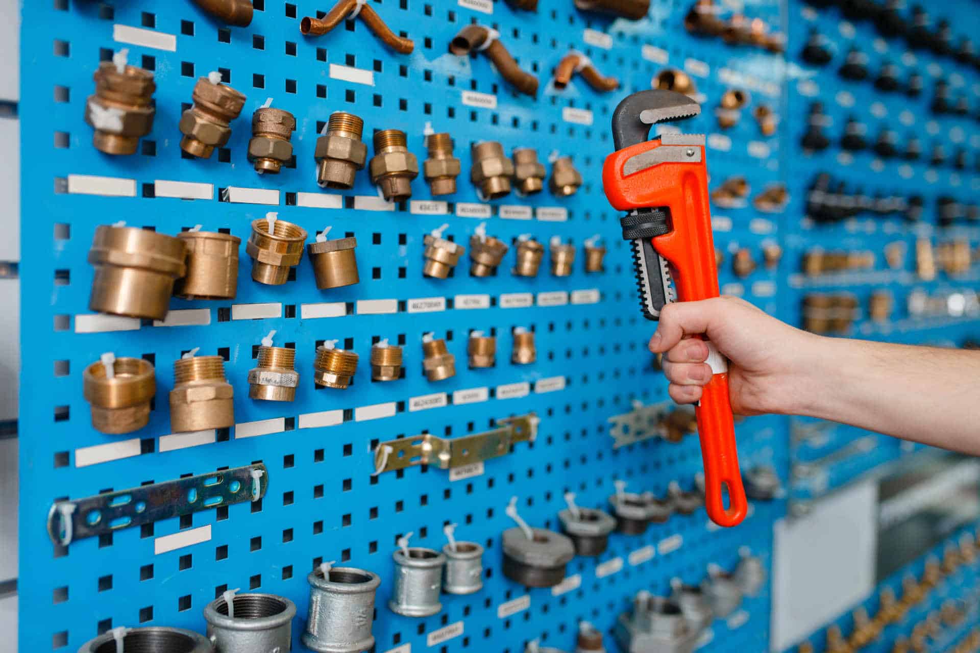 wall of pipe fittings and hand holding pipe wrench.